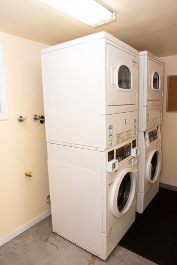 A stack of white front loading washing machines in a laundry room.